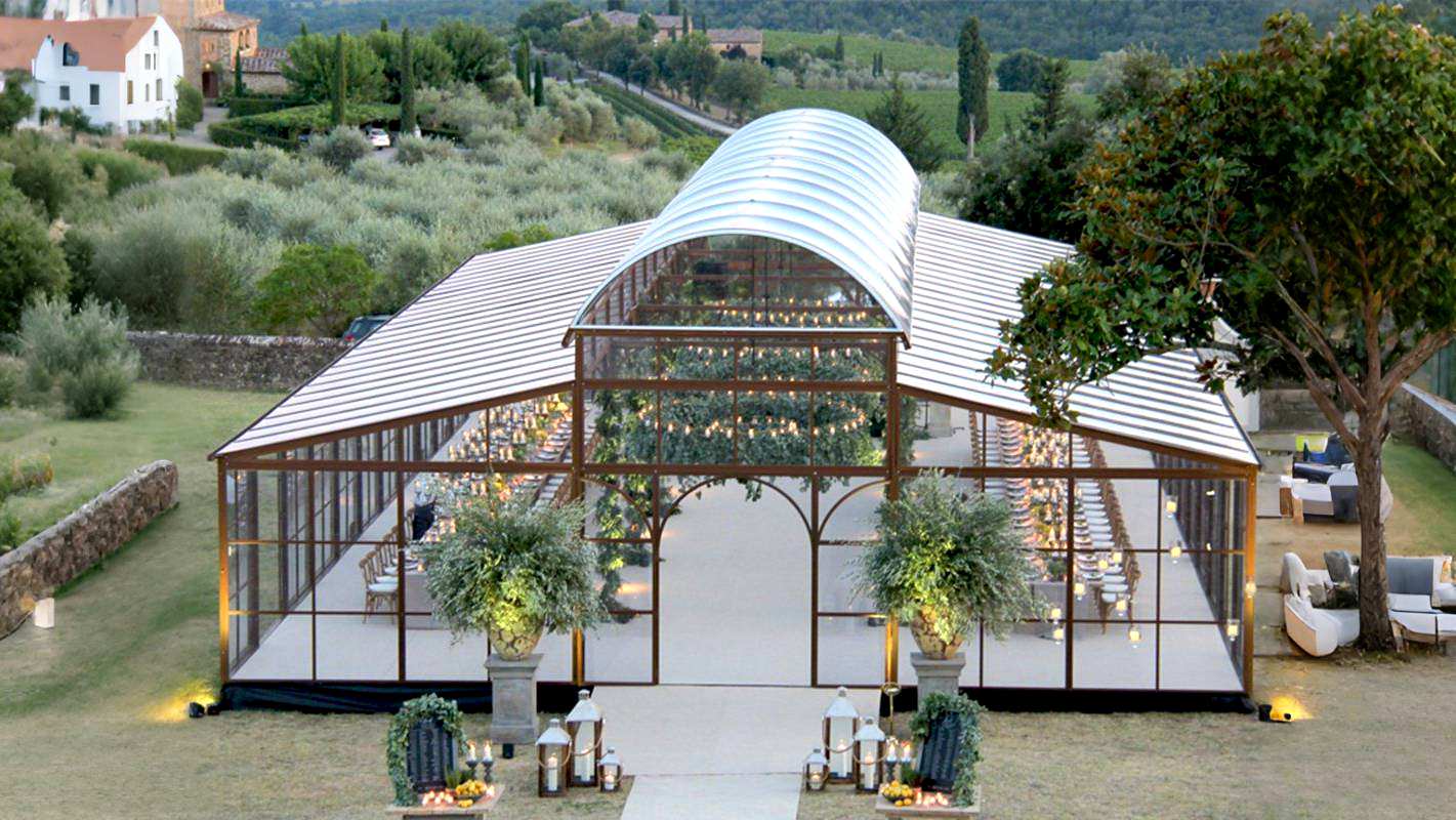 Tuscany style large Victorian glass greenhouse wedding venue, metal frame dome glass sunroom for outdoor banquet and events, countryside landscape backdrop with olive trees and decorative lanterns